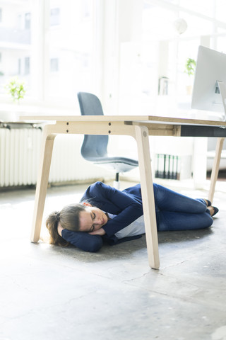 Geschäftsfrau liegt unter dem Tisch im Büro und schläft, lizenzfreies Stockfoto