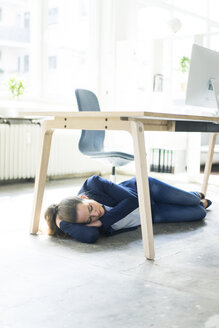 Businesswoman lying under the table in office sleeping - JOSF01775