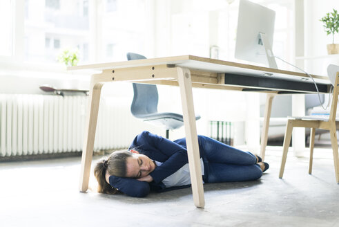 Businesswoman lying under the table in office sleeping - JOSF01776