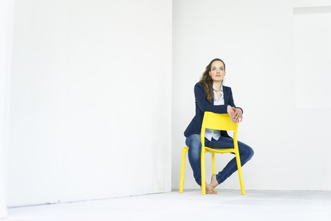 Geschäftsfrau sitzt auf einem gelben Stuhl und denkt nach, lizenzfreies Stockfoto