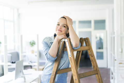 Porträt einer lächelnden Frau, die sich auf eine Leiter stützt, lizenzfreies Stockfoto