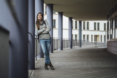 Lächelnde junge Frau lehnt an einer Säule und schaut in die Ferne, lizenzfreies Stockfoto