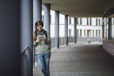 Junge Frau mit Kopfhörern schaut auf Mini-Tablet im Freien - JSCF00004