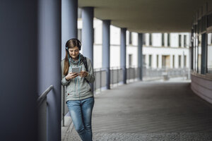 Junge Frau mit Kopfhörern schaut auf Mini-Tablet im Freien - JSCF00004