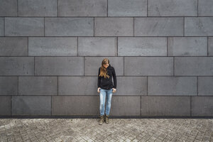 Junge Frau steht vor einer grauen Fassade und schaut nach oben - JSCF00007