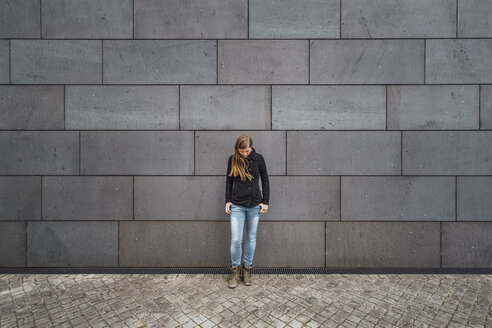 Junge Frau steht vor einer grauen Fassade und schaut nach oben - JSCF00007