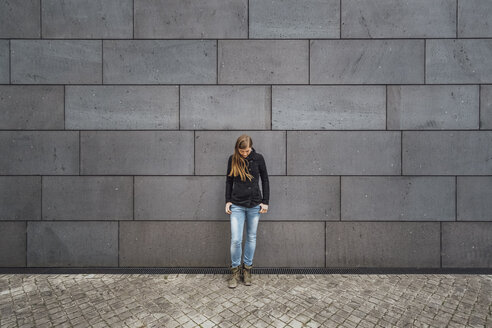 Young woman standing in front of grey facade looking up - JSCF00007