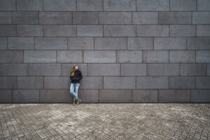 Junge Frau steht vor einer grauen Fassade und wartet - JSCF00008