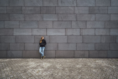 Young woman standing in front of grey facade waiting - JSCF00008