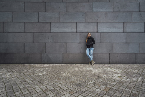 Junge Frau steht vor einer grauen Fassade und wartet - JSCF00009