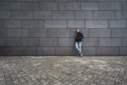 Young woman standing in front of grey facade waiting - JSCF00009