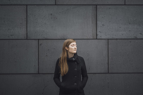 Junge Frau mit geschlossenen Augen vor einer grauen Fassade, lizenzfreies Stockfoto