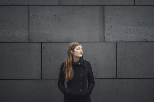 Junge Frau mit geschlossenen Augen vor einer grauen Fassade - JSCF00010