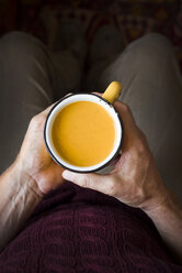 Man's hands holding enamel cup of pumpkin soup - CZF00310