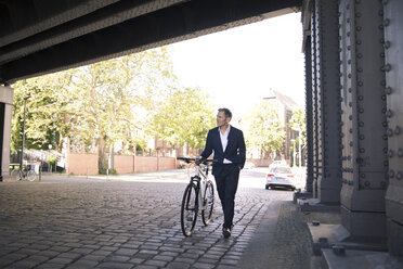 Mature businessman pushing bicycle in the city - FKF02516