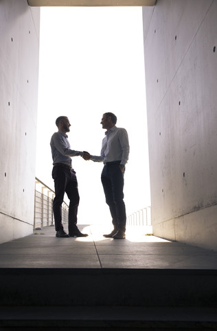 Two businessmen shaking hands in a passageway stock photo