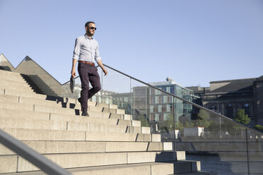 Geschäftsmann mit Sonnenbrille geht eine Treppe hinunter - FKF02537