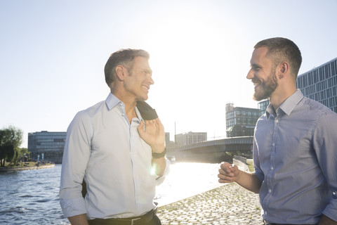 Zwei selbstbewusste Geschäftsleute im Gespräch am Flussufer, lizenzfreies Stockfoto