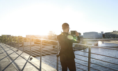 Businessman taking a picture with tablet on a bridge in the city - FKF02547