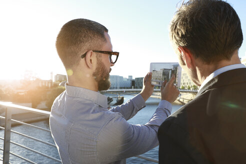 Two businessmen taking a picture with tablet on a bridge in the city - FKF02549