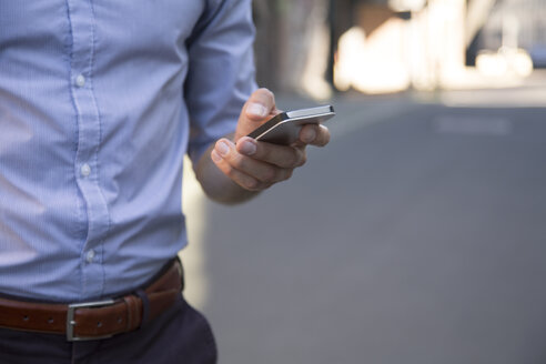 Nahaufnahme eines Geschäftsmannes, der ein Mobiltelefon hält - FKF02562