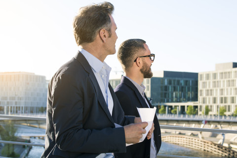 Zwei Geschäftsleute auf einer Brücke in der Stadt schauen sich um, lizenzfreies Stockfoto