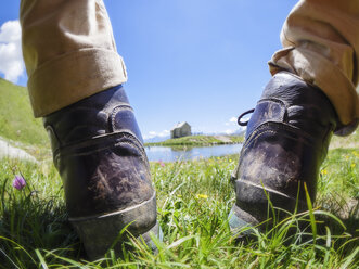 Italy, South Tyrol, Sesvenna Alps, close-up of hiking boots in front of Pforzheim mountain hut and lake - LAF01901