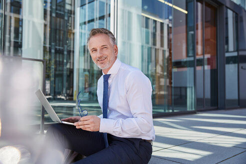 Porträt eines lächelnden Geschäftsmannes, der einen Laptop im Freien benutzt - SUF00288