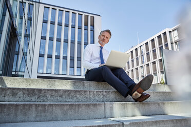 Porträt eines Geschäftsmannes, der auf einer Treppe sitzt und einen Laptop benutzt - SUF00290