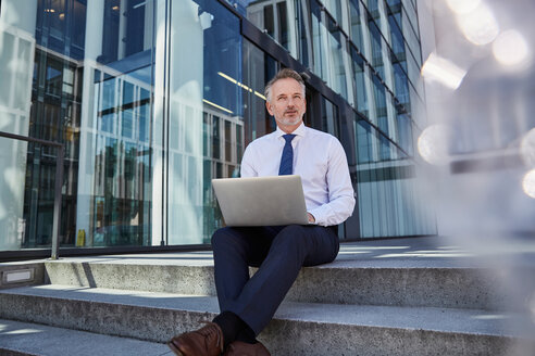 Porträt eines Geschäftsmannes mit Laptop auf einer Treppe sitzend - SUF00291