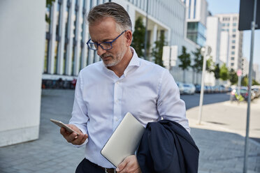 Geschäftsmann mit Laptop und Blick auf das Mobiltelefon - SUF00298