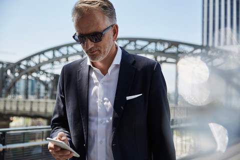 Deutschland, München, Porträt eines Geschäftsmannes mit Sonnenbrille, der auf sein Handy schaut, lizenzfreies Stockfoto