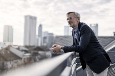 Grauhaariger Geschäftsmann steht auf einem Balkon und blickt über die Stadt - SBOF00731