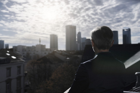 Grauhaariger Geschäftsmann auf Balkon mit Blick über die Stadt, lizenzfreies Stockfoto