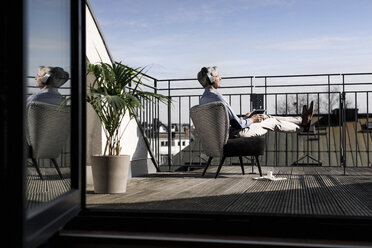 Grauhaariger Mann entspannt sich im Stuhl auf dem Balkon - SBOF00736