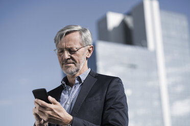 Grey-haired businessman typing into smartphone - SBOF00738