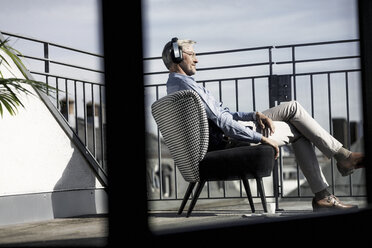 Grauhaariger Mann entspannt sich im Stuhl auf dem Balkon und hört Musik - SBOF00739