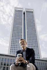 Grey-haired businessman in front of skyscraper holding coffee to go - SBOF00744