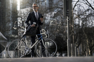 Grey-haired businessman with bicycle and coffee to go in the city - SBOF00748
