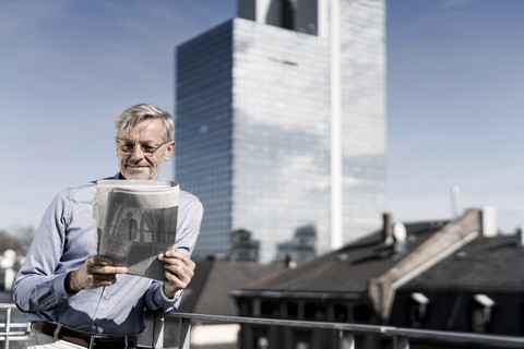 Grauhaariger Mann auf dem Balkon liest Zeitung, lizenzfreies Stockfoto