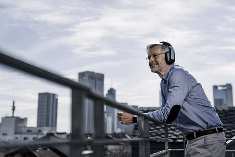 Grauhaariger Mann mit Kopfhörern genießt die Aussicht auf die Stadt, lizenzfreies Stockfoto