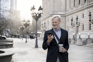 Grauhaariger Geschäftsmann in der Stadt mit Smartphone und Kaffee zum Mitnehmen - SBOF00764