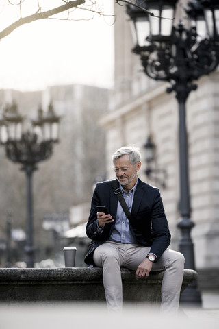 Grauhaariger Geschäftsmann in der Stadt mit Smartphone und Kaffee zum Mitnehmen, lizenzfreies Stockfoto