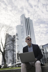 Grauhaariger Geschäftsmann mit Sonnenbrille arbeitet mit Laptop im Park - SBOF00770