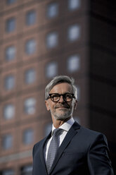 Grey-haired businessman in front of red skyscraper - SBOF00776