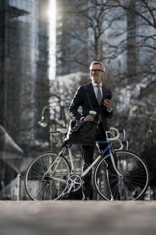Grey-haired businessman with bicycle and coffee to go in the city stock photo