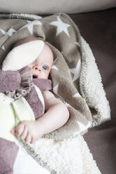 Porträt eines in eine Decke eingewickelten kleinen Mädchens, das auf einer Couch liegt - CSTF01403