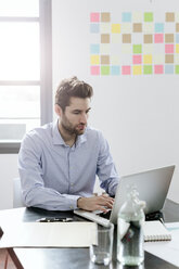 Junger Geschäftsmann bei der Arbeit im Büro, mit Laptop - GIOF03238