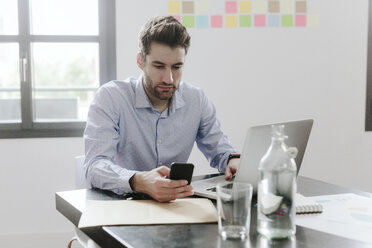 Young businessman working in office, using smartphone and laptop - GIOF03240