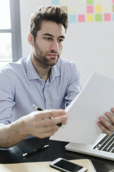 Young businessman working in office, reading documents - GIOF03243